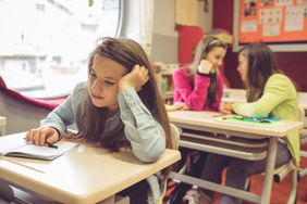 Girl in school looking unhappy while other girls gossip behind her.