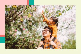 Little girls sitting on her dad's shoulders reaching for a flower