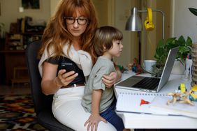 Mother texts with her son sitting on her lap and looking at a computer. 