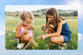 Two playful girls look through a magnifying glass while playing in the field, surrounded by nature.