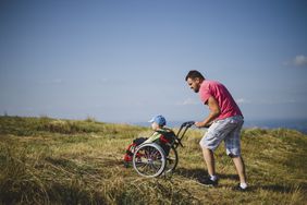 Father pushing child in wheelchair at the top of seaside hill.