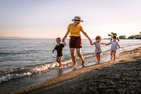 Mid adult woman at beach walk in sunset with three children. Running and having fun on the beach.