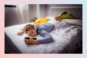 Teenager laying on the bed looking at a phone with headphones on.