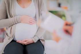 Pregnant Woman Holding Stomach Sitting in Doctors Office