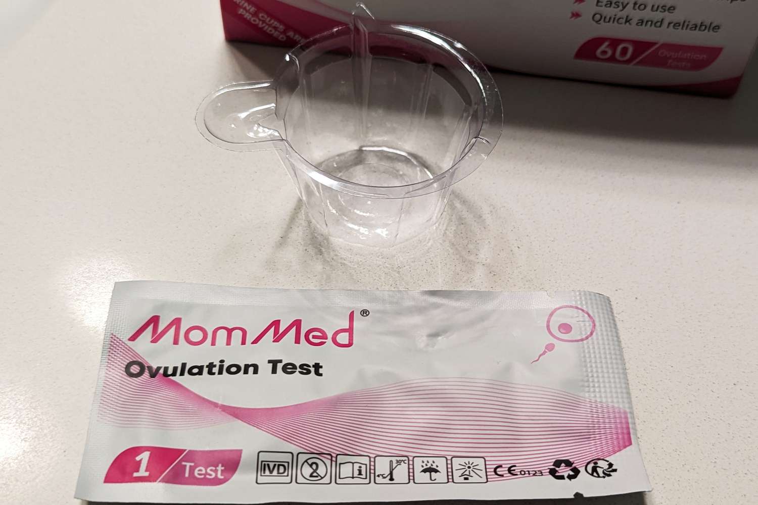 MomMed Ovulation Test Strip in its packaging and siting on a counter next to a plastic cup