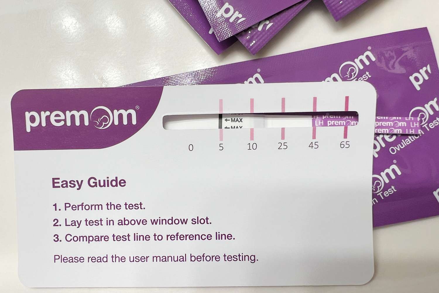 Premom Quantitative Ovulation Test Strip sitting atop its packaging with an instructional card atop that