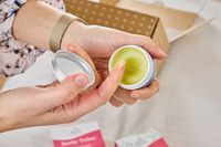 A person examines the texture of the organic perineal balm included in the Earth Mama Postpartum Recovery Collection