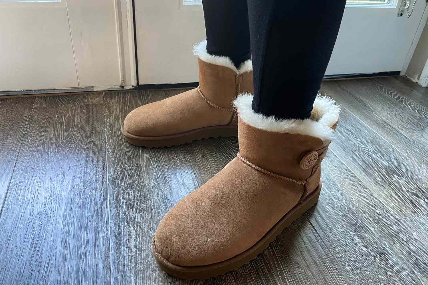 The UGG Mini Bailey Button II Boots worn on a wooden floor