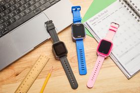 Three smart watches on a desk next to a laptop and daily planner.