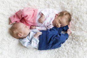 Newborn baby girl and boy in pink and blue outfits laying on white carpet.