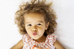 Girl wearing polka dots with curly brown hair and puckered lips looking at the camera