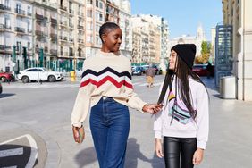 Smiling mom and her daughter talking while walking together along a street in the city in summer