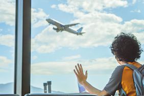 Kid looking out of airport window, waiting for his flight