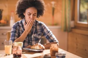 Young African American woman feeling nausea during breakfast time at dining room.