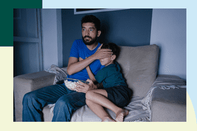 Father covering his son's eyes as they sit in front of a screen